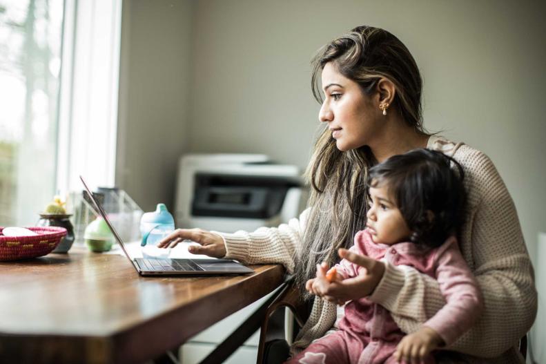 Una mujer trabaja en su computadora mientras cuida de su bebe 