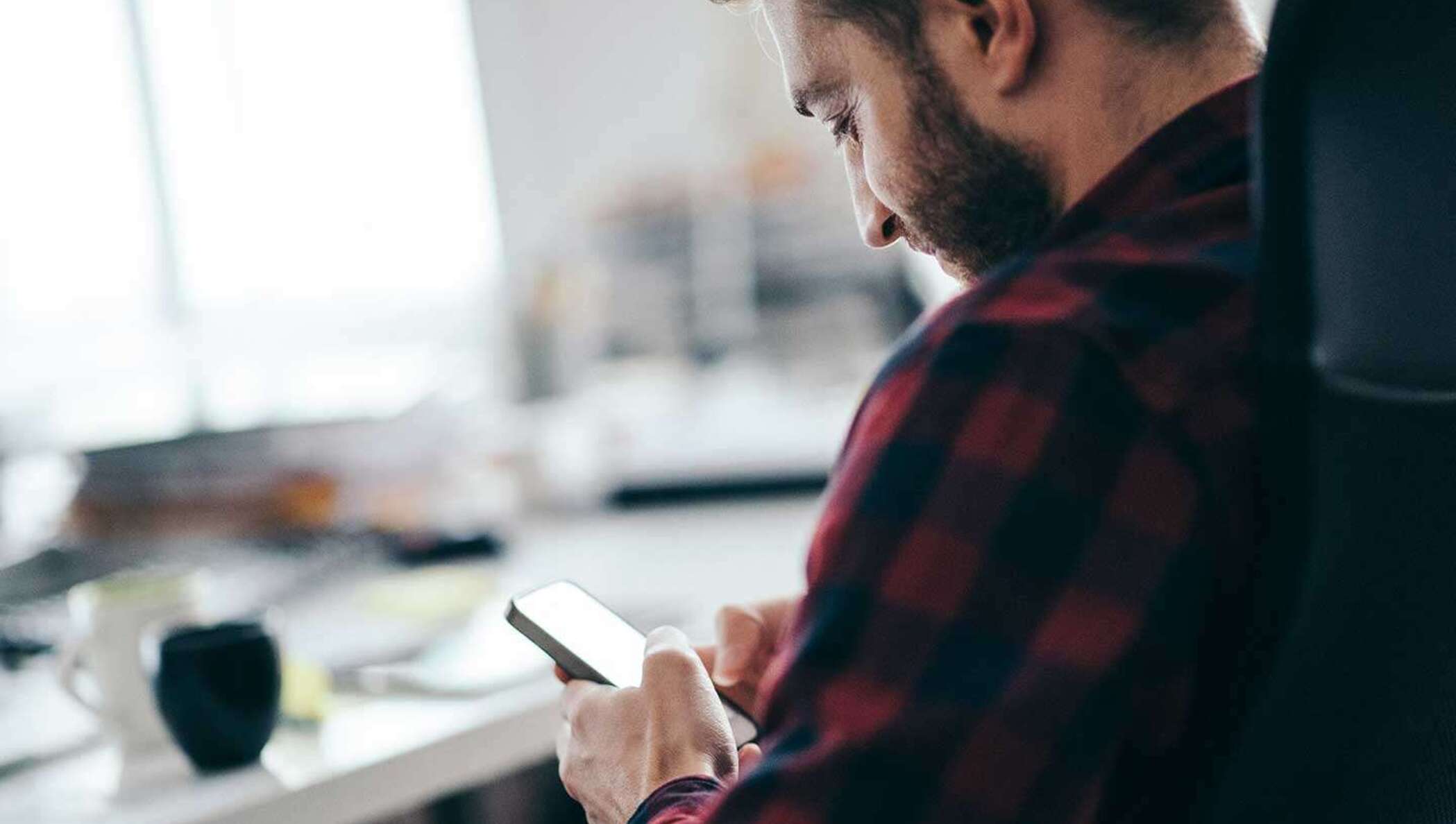 Ein Mann mit Bart im Flanellhemd prüft auf seinem Mobiltelefon den Status eines zur Unterschrift ausliegenden Dokuments